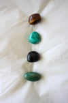 This image shows the four tumble stones of the Taurus Zodiac Crystal Kit, which are (from top to bottom): brown and yellow Tigers Eye, green Malachite, Black Tourmaline and green Aventurine. 