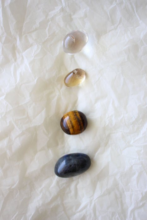 This image shows the four tumble stones of the Gemini Zodiac Crystal Kit, which are (from top to bottom): Clear Quartz, yellow Citrine, brown and yellow Tigers Eye and green Aventurine.  