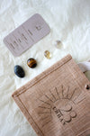  This image shows the 23 Urban Gemini Zodiac Kit in flat lay. To the bottom right of the picture is the 23 Urban jute bag which all products come in. Then are the four Gemini tumble stones, which are Clear Quartz, yellow Citrine, brown and yellow Tigers Eye and Labradorite. Next to the tumble stones on the top left is the Gemini Zodiac Crystal Kit card, outlining the traits of Gemini and explaining the properties of the crystals. 