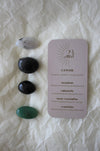 To the left of this image are the four Cancer Zodiac Crystal Kit tumble stones, which are Moonstone, Labradorite, Black Tourmaline and green Aventurine. Next to the tumble stones is a Cancer Zodiac Crystal Kit card, outlining the traits of Cancer and explaining the properties of the crystals. 
