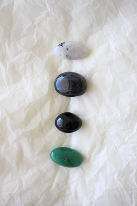 This image shows the four tumble stones of the Gemini Zodiac Crystal Kit, which are (from top to bottom): Moonstone, Labradorite, Black Tourmaline and green Aventurine.