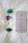 To the left of this image are the four Virgo Zodiac Crystal Kit tumble stones, which are Amazonite, Amethyst, Clear Quartz and Aventurine. Next to the tumble stones is a Virgo Zodiac Crystal Kit card, outlining the traits of Virgo and explaining the properties of the crystals. 