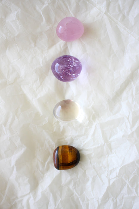 This image shows the four tumble stones of the Libra Zodiac Crystal Kit, which are (from top to bottom): Rose Quartz, Amethyst, Clear Quartz and Tigers Eye