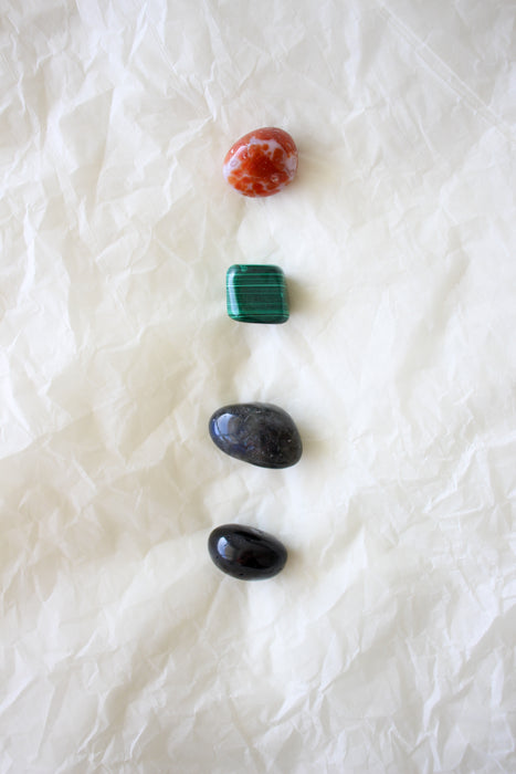 This image shows the four tumble stones of the Scorpio Zodiac Crystal Kit, which are (from top to bottom): Carnelian, Malachite, Labradorite and Black Tourmaline