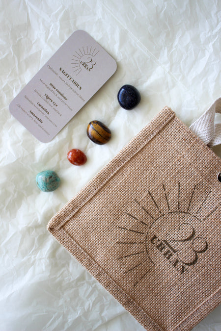  This image shows the 23 Urban Sagittarius Zodiac Kit in flat lay. On the bottom right is the 23 Urban jute bag which all products come in. Then are the four Sagittarius tumble stones, which are Blue Sunstone, Tigers Eye, Carnelian and Amazonite. Next to the tumble stones on the bottom right is the Sagittarius Zodiac Crystal Kit card, outlining the traits of Sagittarius and explaining the properties of the crystals. 