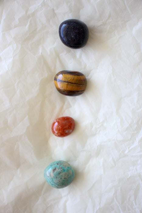 This image shows the four tumble stones of the Sagittarius Zodiac Crystal Kit, which are (from top to bottom): Blue Sunstone, Tigers Eye, Carnelian and Amazonite