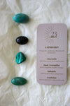 To the left of this image are the four Capricorn Zodiac Crystal Kit tumble stones, which are Amazonite, Black Tourmaline, Malachite, Aventurine. Next to the tumble stones is a Capricorn Zodiac Crystal Kit card, outlining the traits of Capricorn and explaining the properties of the crystals. 