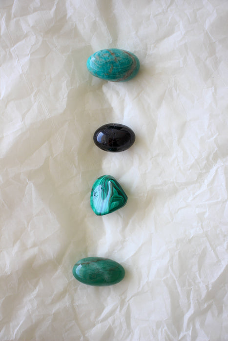 This image shows the four tumble stones of the Capricorn Zodiac Crystal Kit, which are (from top to bottom): Amazonite, Black Tourmaline, Malachite, Aventurine