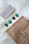 This image shows the 23 Urban Capricorn Zodiac Kit in flat lay. On the bottom right is the 23 Urban jute bag which all products come in. Then are the four Capricorn tumble stones, which are Amazonite, Black Tourmaline, Malachite, Aventurine. Next to the tumble stones on the bottom right is the Capricorn Zodiac Crystal Kit card, outlining the traits of Capricorn and explaining the properties of the crystals. 