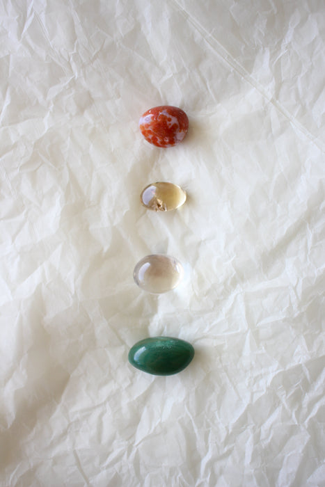 A flat lay of the four Aries tumble stones that come in the Zodiac Crystal Kit. They are  red Carnelian, yellow Citrine, Clear Quartz and green Aventurine