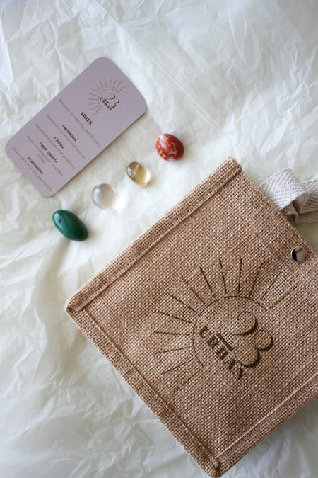 The 23 Urban Aries Zodiac Crystal Kit as a flat lay, showing the Zodiac card that comes with the kit, the four tumble stones for Aries (Carnelian, Citrine, Clear Quartz and Aventurine) and the 23 Urban branded jute gift bag.  