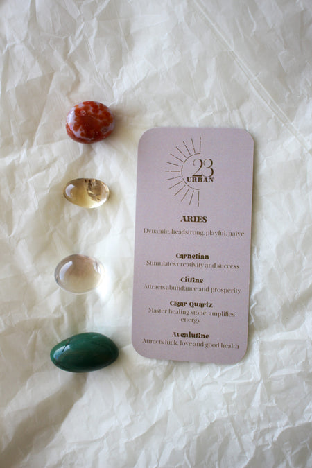 A flat lay of the four Aries tumble stones (Carnelian, Citrine, Clear Quartz and Aventurine) next to the Zodiac crystal kit card 