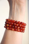 Four Carnelian crystal bracelets in a stack against a white background. 