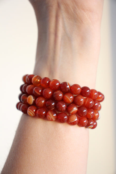 Four Carnelian crystal bracelets in a stack against a white background. 