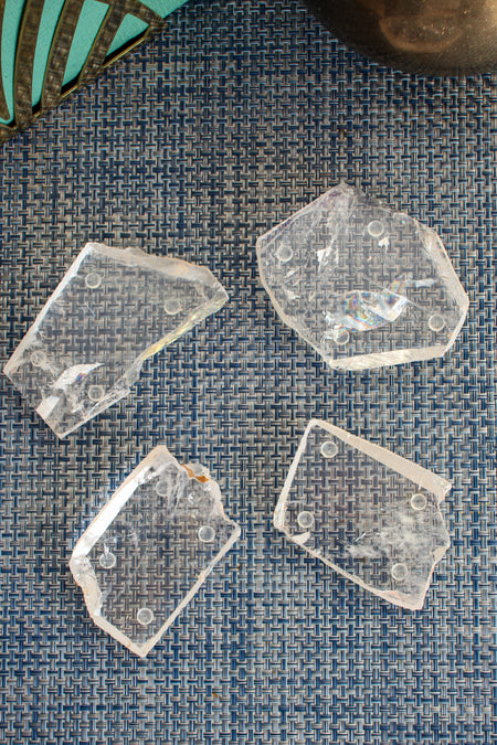 A set of four Clear Quartz Coasters, shot from above. The coasters are on a blue woven placemat