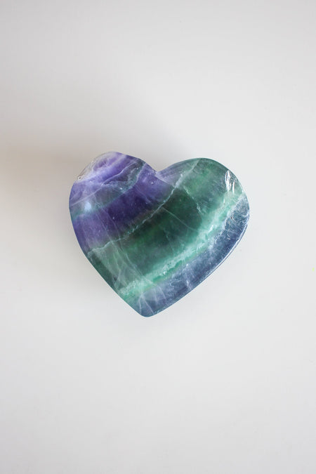 A close up shot of a heart shaped Rainbow fluorite bowl, coloured with blue, green and purple stripes. 