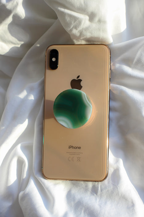 Green circular Agate Crystal Phone Grip on the back of a rose gold iPhone on a white background