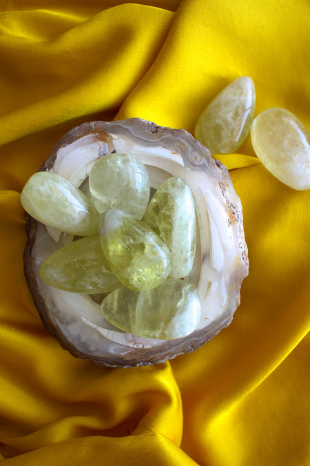 A bowl of lemon yellow citrine palm stones sits on a yellow background 