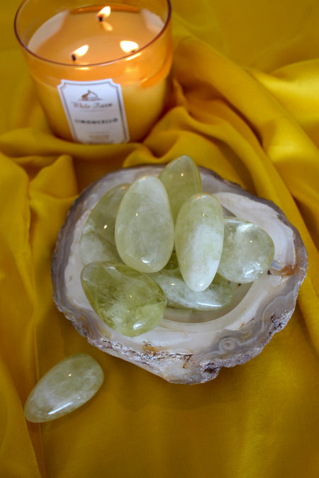 A bowl of lemon yellow Citrine palm stones sits on a yellow cloth. In the background is a yellow candle