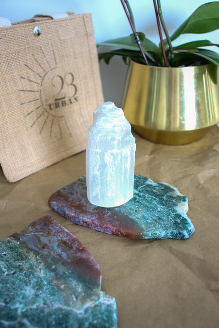 A small Selenite Tower sits on a red and blue Ocean Jasper slab on a brown table