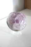 A beautiful Uruguayan Amethyst Sphere sits on a white bookshelf in the afternoon sun 