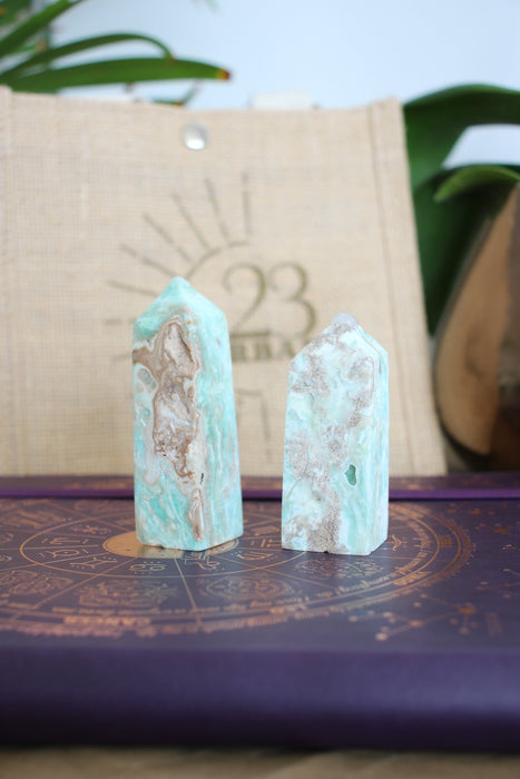 Two pale blue and soft brown Caribbean Calcite towers sit on a purple book, in front of a 23 Urban branded jute bag