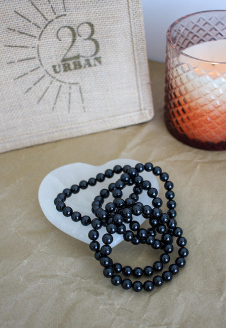 A stack of shiny Black Tourmaline bracelets in a heart shaped selenite bowl