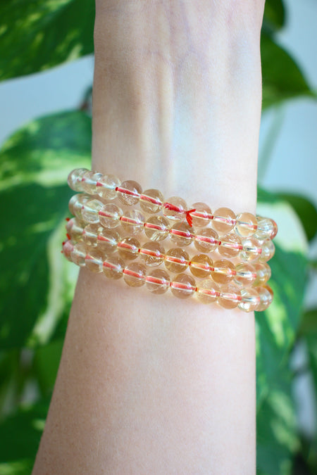 A stack of bright yellow Citrine bracelets on a wrist in front of a green plant 