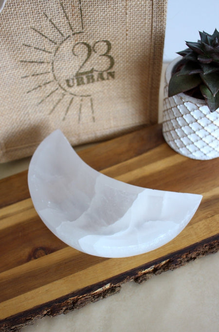 A white selenite moon shaped bowl sits on a brown table 