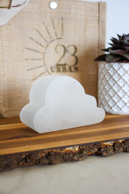 A cloud shaped white selenite cleansing plate sits upright on a brown table 