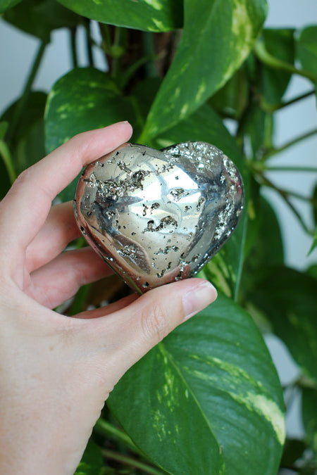 A golden Pyrite heart is held in front of a tree
