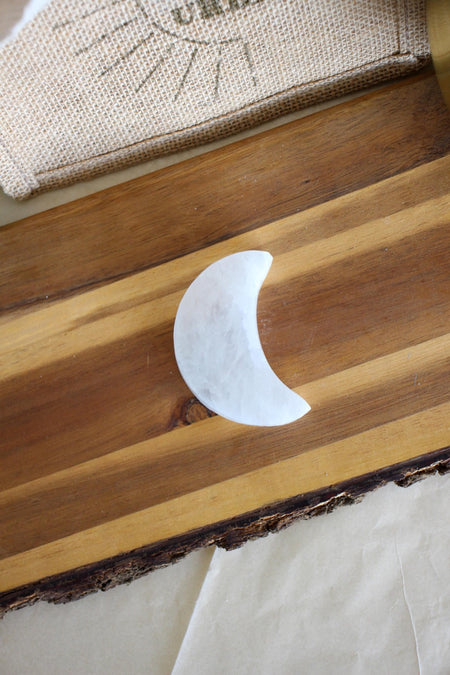 Moon shaped white selenite charging plate on a brown wooden table