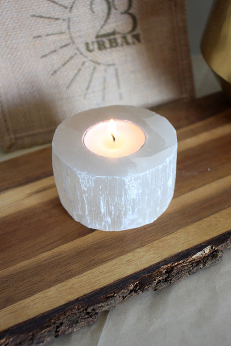 A white selenite tea light holder with a lit candle inside it