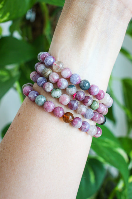 Beautiful pink tourmaline bracelets stacked on a wrist in front of a green plant 