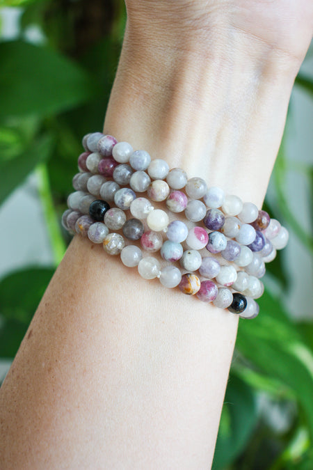A stack of beautiful small bead pale Pink Tourmaline bracelets on a wrist in front of a green plant.