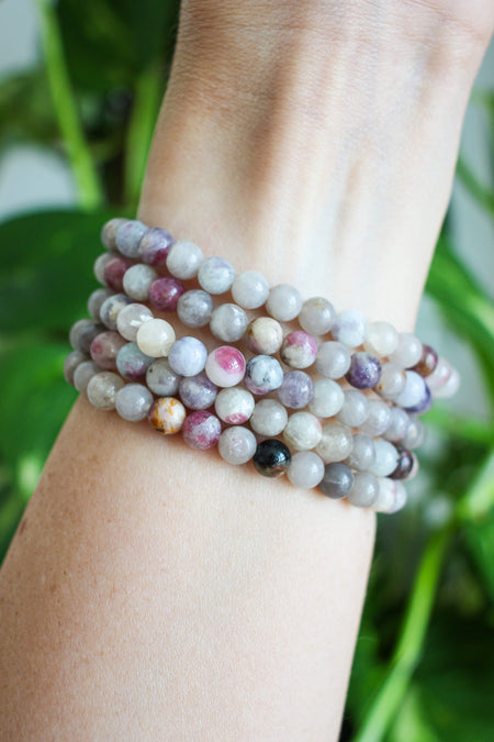 A stack of beautiful small bead pale Pink Tourmaline bracelets on a wrist in front of a green plant.