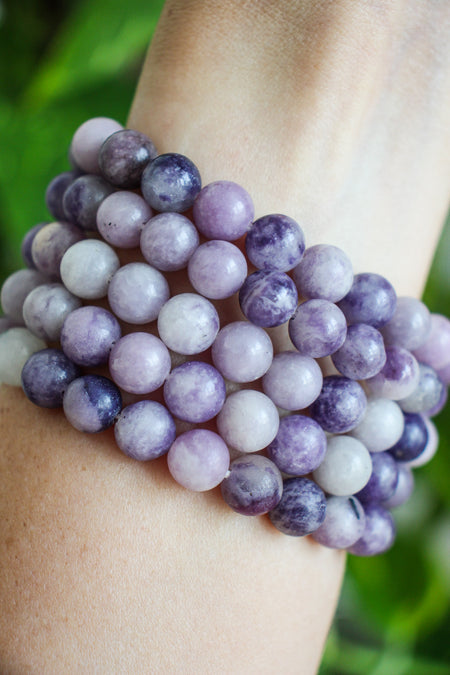 Lilac coloured lepidolite stack on a wrist in front of a green tree