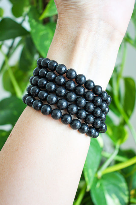 Matte black Shungite Bracelets stacked on a wrist in front of a green plant 