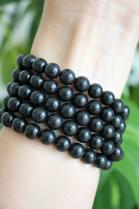Matte black Shungite Bracelets stacked on a wrist in front of a green plant 