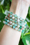 A stack of Green Flower Agate bracelets on a wrist in front of a green plant 