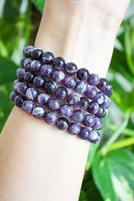 Juicy Purple Dream Amethyst bracelets stacked on a wrist in front of a  green plant background