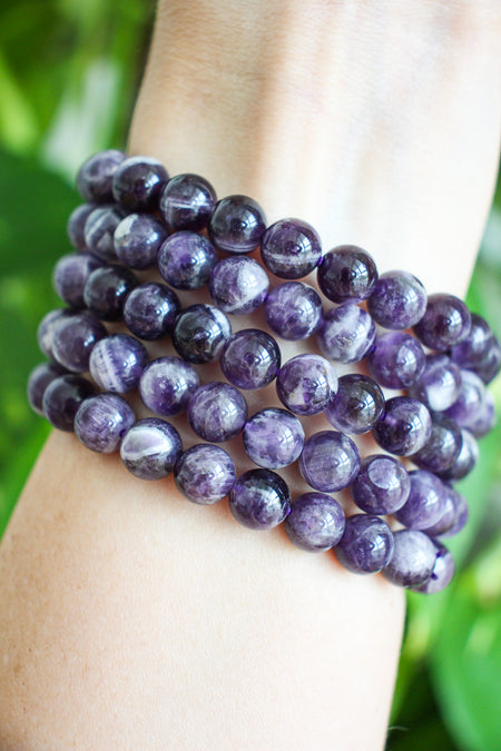 Juicy Purple Dream Amethyst bracelets stacked on a wrist in front of a  green plant background