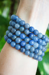 A stack of Blue Aventurine bracelets in a bright sky blue colour, on a wrist in front of a green plant. 