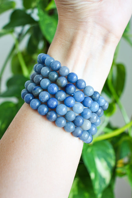 A stack of Blue Aventurine bracelets in a bright sky blue colour, on a wrist in front of a green plant. 