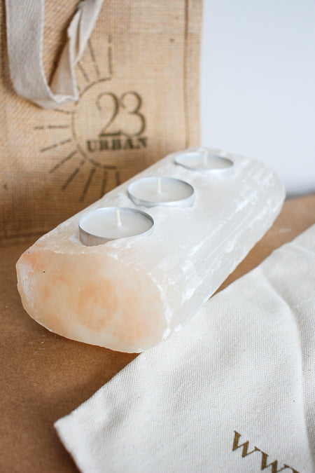 A Selenite log tea light holder, feature three shallow holes for tea lights. The Selenite is white but also shows blush peach tones, typical of Selenite from Morocco. Dubai Crystals. 23 Urban,