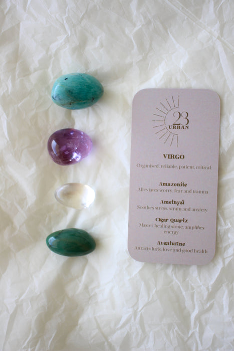 To the left of this image are the four Virgo Zodiac Crystal Kit tumble stones, which are Amazonite, Amethyst, Clear Quartz and Aventurine. Next to the tumble stones is a Virgo Zodiac Crystal Kit card, outlining the traits of Virgo and explaining the properties of the crystals. 