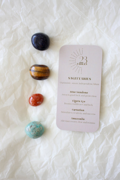  To the left of this image are the four Sagittarius Zodiac Crystal Kit tumble stones, which are Blue Sunstone, Tigers Eye, Carnelian and Amazonite. Next to the tumble stones is a Sagittarius Zodiac Crystal Kit card, outlining the traits of Sagittarius and explaining the properties of the crystals. 