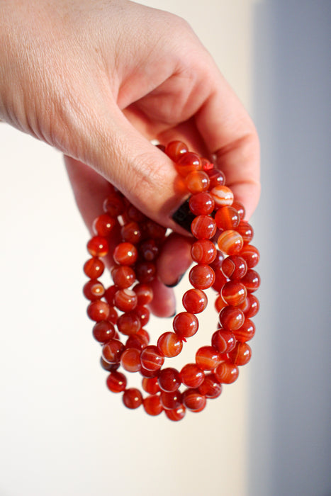 Four Carnelian crystal bracelets against a white background.