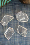 A set of four Clear Quartz Coasters, shot from above. The coasters are on a blue woven placemat