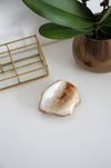 A cream and orange agate bowl sits on a white table in front of an orchid plant